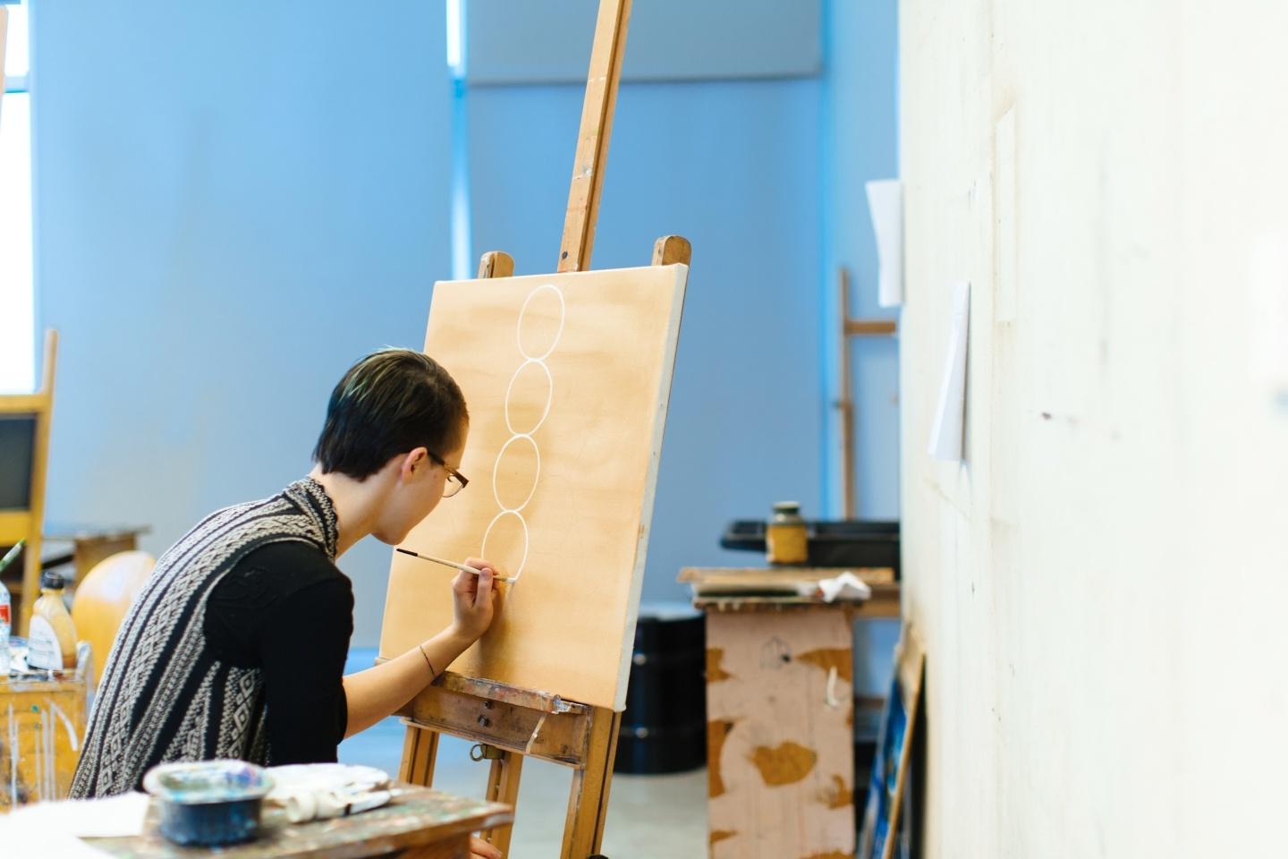 一个学生在自然采光的艺术工作室里在画布上画圆圈